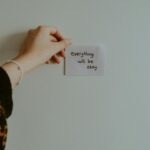 kobieta przyklejająca na ścianie karteczkę z napisem "Everything will be okay"