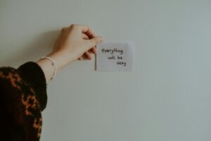 kobieta przyklejająca na ścianie karteczkę z napisem "Everything will be okay"