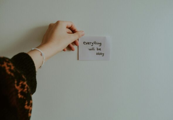 kobieta przyklejająca na ścianie karteczkę z napisem "Everything will be okay"