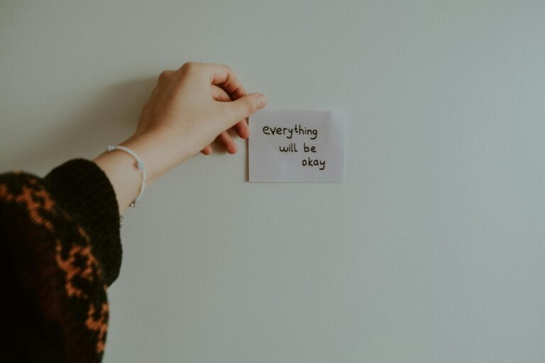 kobieta przyklejająca na ścianie karteczkę z napisem "Everything will be okay"