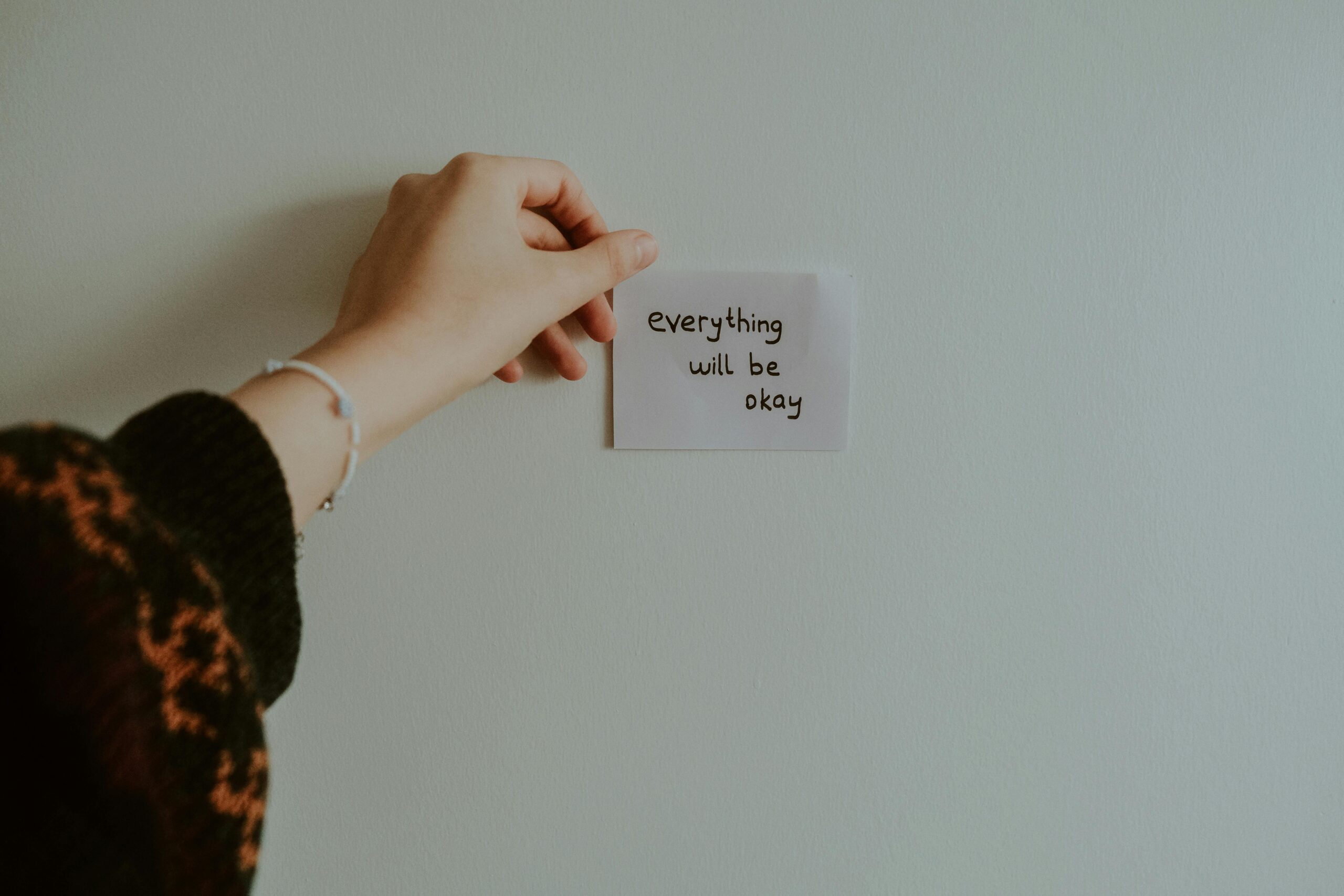 kobieta przyklejająca na ścianie karteczkę z napisem "Everything will be okay"