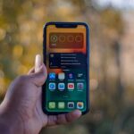 Dłoń trzymająca smartfon z widocznym ekranem głównym i widżetem baterii.