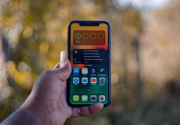 Dłoń trzymająca smartfon z widocznym ekranem głównym i widżetem baterii.