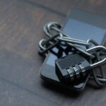 Smartfon owinięty metalowym łańcuchem zapiętym na czarną kłódkę szyfrową na drewnianym stole.
