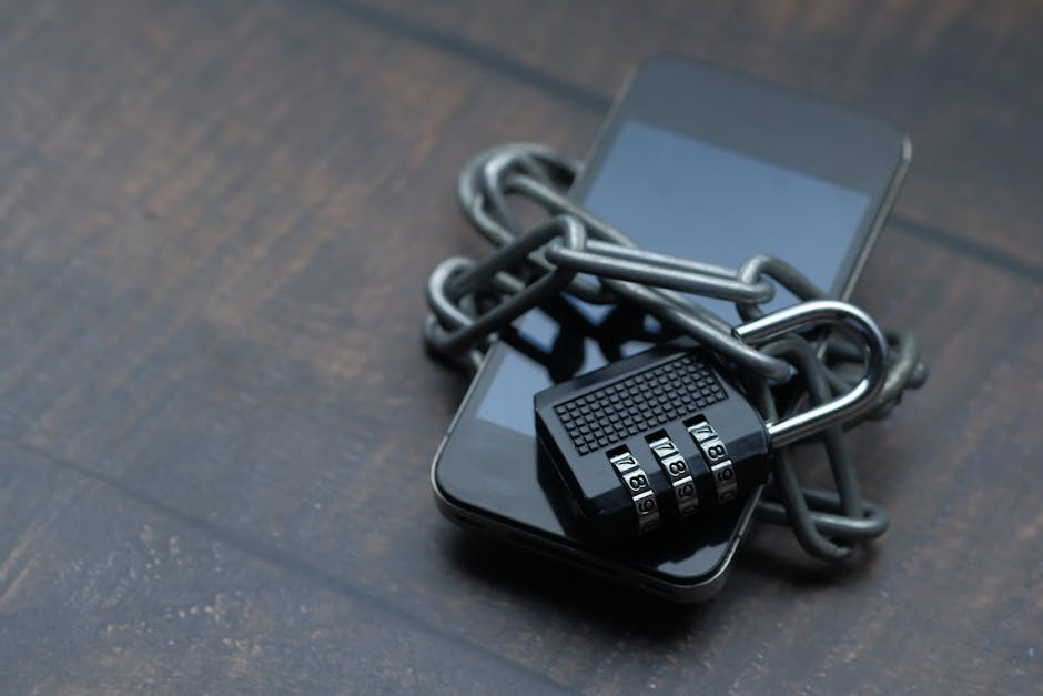 Smartfon owinięty metalowym łańcuchem zapiętym na czarną kłódkę szyfrową na drewnianym stole.