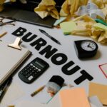 Biurko z napisem „Burnout”, kalkulatorem, zegarem i wieloma pogniecionymi kartkami papieru.
