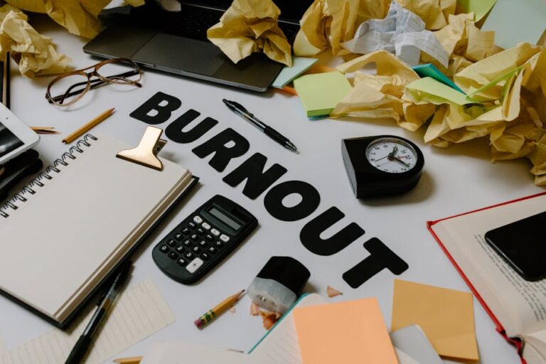 Biurko z napisem „Burnout”, kalkulatorem, zegarem i wieloma pogniecionymi kartkami papieru.