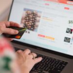 kobieta siedząca przed laptopem z kartą płatniczą w ręku