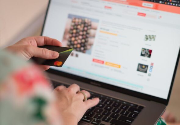 kobieta siedząca przed laptopem z kartą płatniczą w ręku