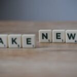 Napis „FAKE NEWS” ułożony z płytek do gry w literki na drewnianym blacie.