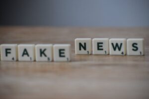 Napis „FAKE NEWS” ułożony z płytek do gry w literki na drewnianym blacie.
