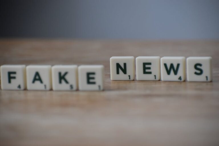 Napis „FAKE NEWS” ułożony z płytek do gry w literki na drewnianym blacie.