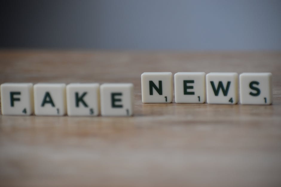 Napis „FAKE NEWS” ułożony z płytek do gry w literki na drewnianym blacie.