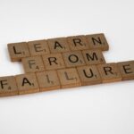 Napis „LEARN FROM FAILURE” ułożony z drewnianych klocków do gry w Scrabble.
