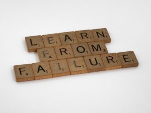 Napis „LEARN FROM FAILURE” ułożony z drewnianych klocków do gry w Scrabble.