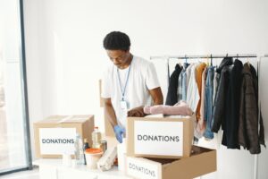 Mężczyzna w białej koszulce sortuje rzeczy w kartonach z napisem „DONATIONS”.