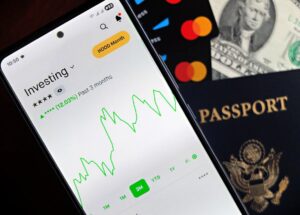 Smartfon z wykresem giełdowym, paszport oraz karty płatnicze na blacie.