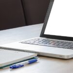 otwarty laptop z białym ekranem, notatnik i długopis
