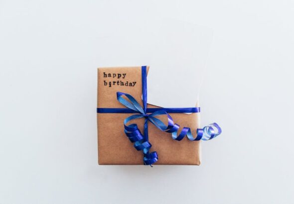 Prezent w brązowym papierze owinięty niebieską wstążką z napisem „happy birthday”.