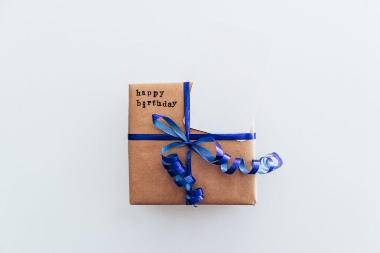 Prezent w brązowym papierze owinięty niebieską wstążką z napisem „happy birthday”.