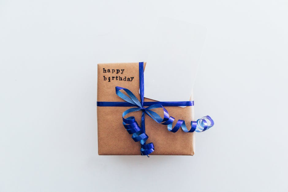 Prezent w brązowym papierze owinięty niebieską wstążką z napisem „happy birthday”.