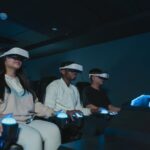 Trzy osoby w goglach VR siedzą w fotelach i trzymają świecące kontrolery.