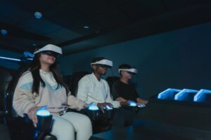 Trzy osoby w goglach VR siedzą w fotelach i trzymają świecące kontrolery.